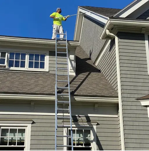 Crew power washing a house exterior from a ladder